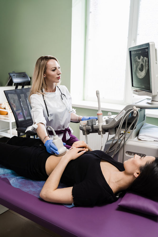 Gynecologist Conducts Ultrasound Scan For Pregnant Young Woman On Early Pregnancy Period And Look On The Screen In Hospital. Pregnancy And Maternity.